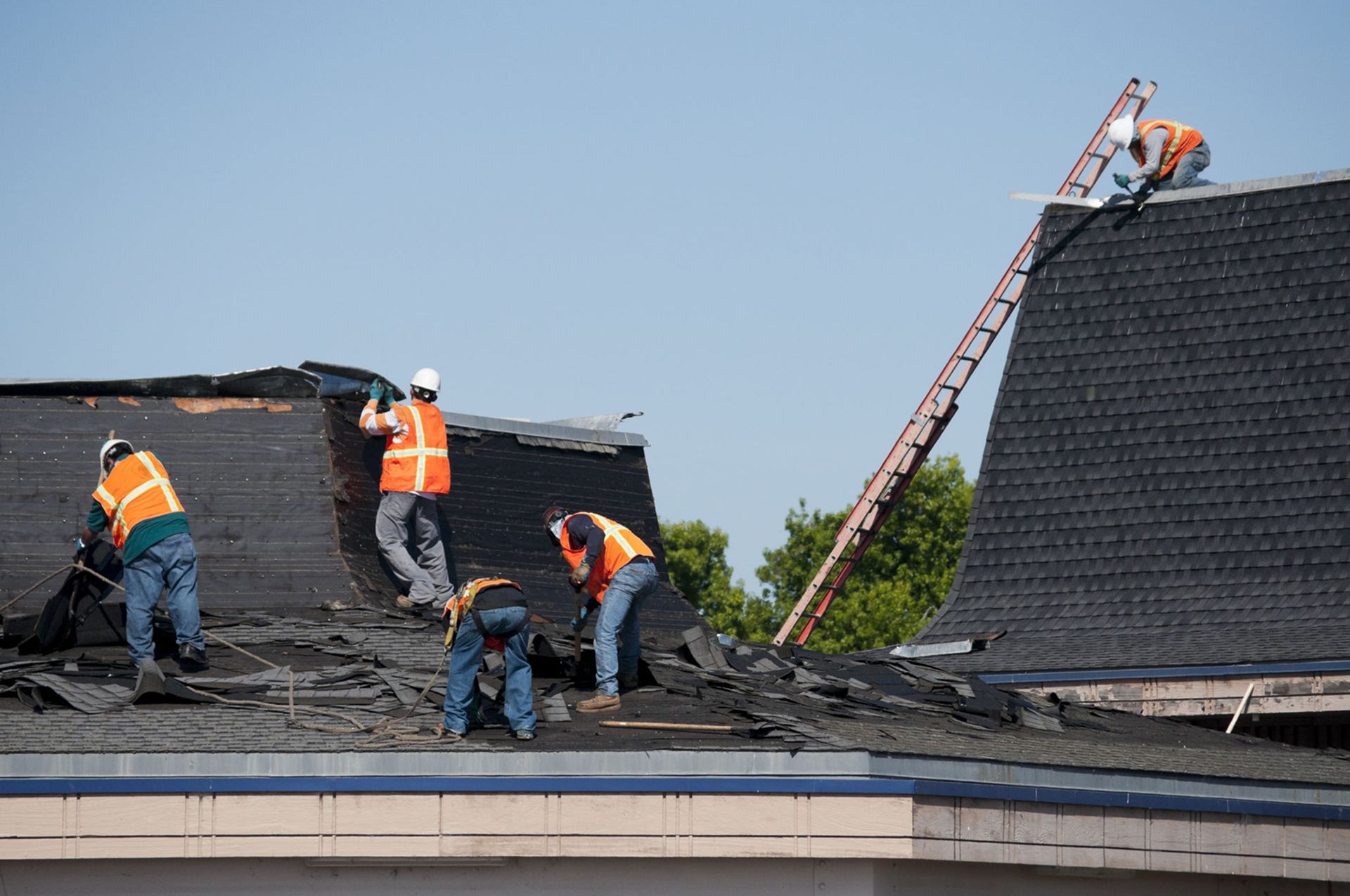 Workers repairing roof with safety equipment.